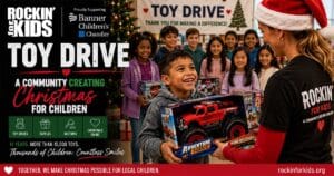 Volunteer presents a Christmas toy to a smiling child during Rockin' for Kids' annual Toy Drive, bringing joy and hope to local children.